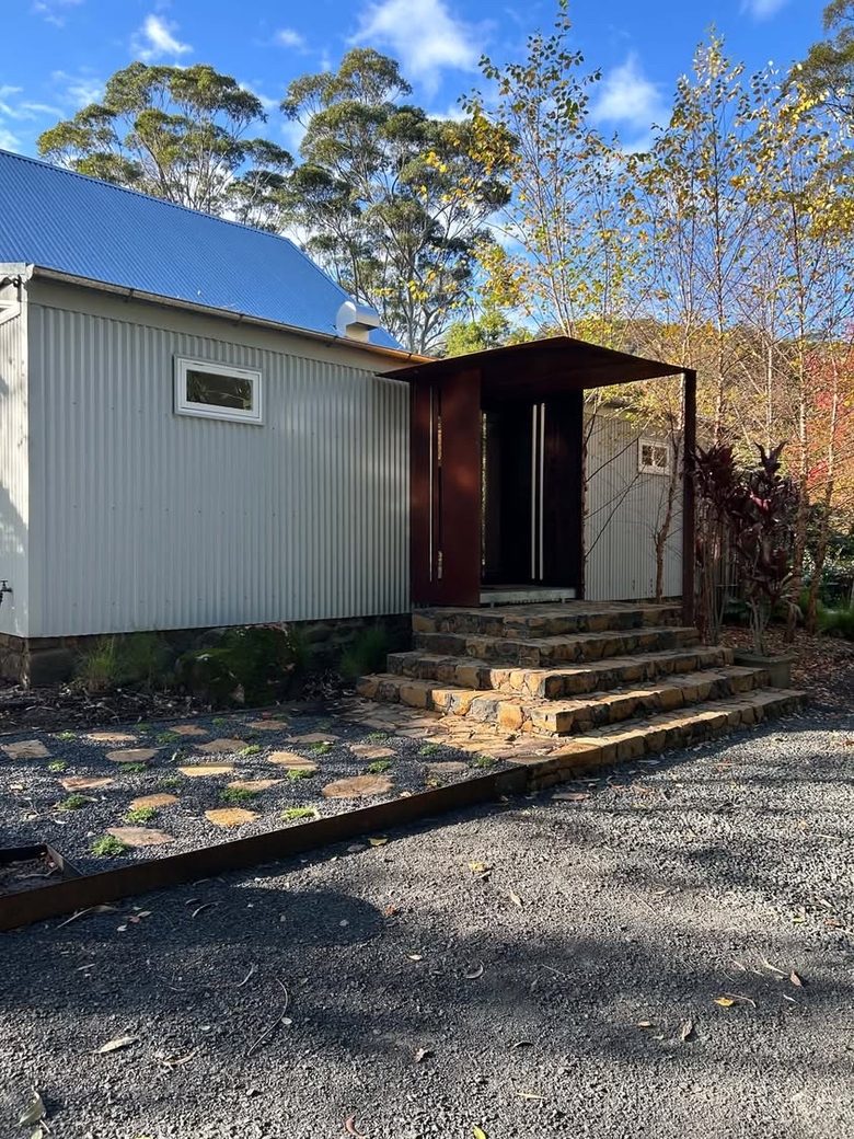 Custom COR-TEN steel entry portal framing the front door of a home, above stone steps.