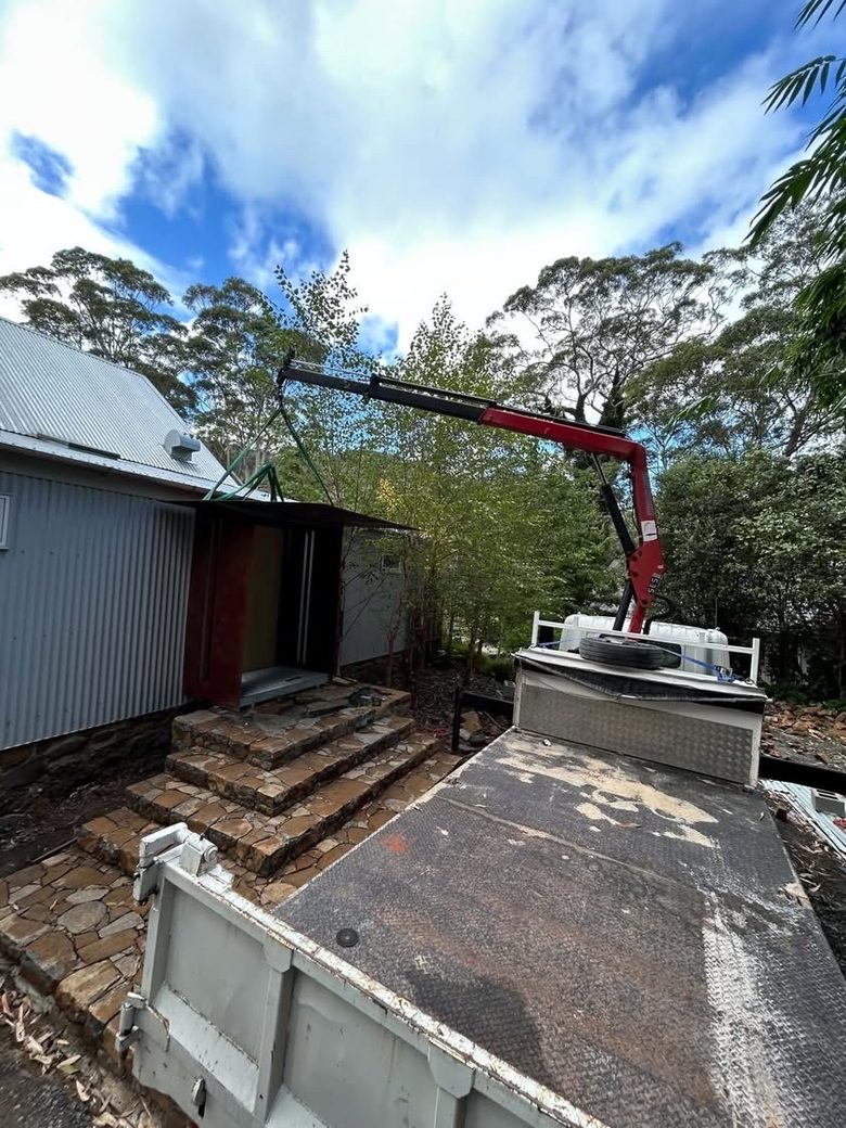 Truck-mounted crane lifting a COR-TEN steel entry structure into place on site.