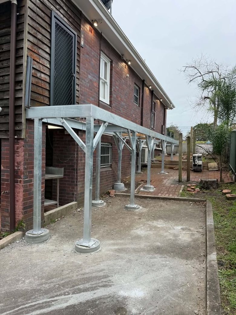 Hot-dip galvanised steel subframe with braced posts installed along the side of a brick home.