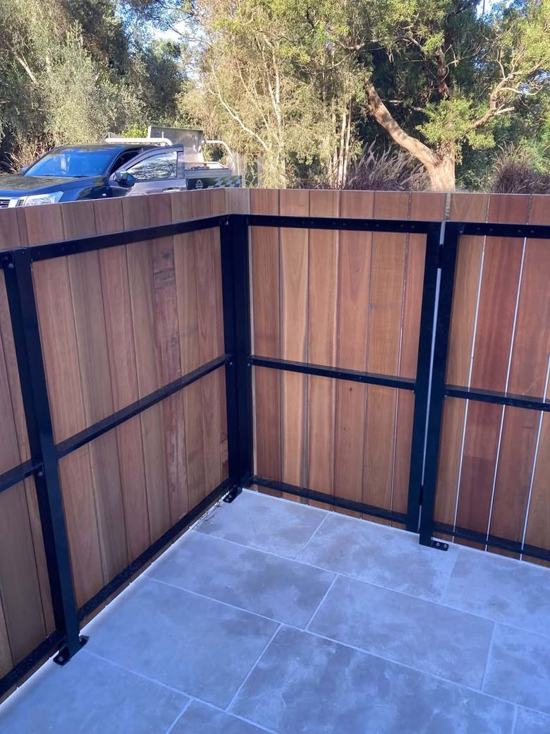 Black steel frame fabricated to carry a hardwood privacy screen, installed over travertine paving.
