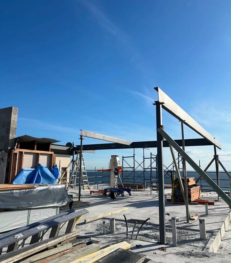 Fabricated steel portal frame standing against a clear sky on a coastal build, ocean behind.