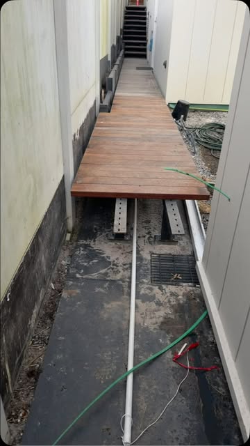 Steel bearers laid for a narrow side-passage walkway with timber decking being fitted over the top.