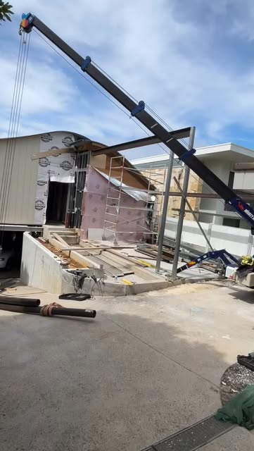 Truck-mounted crane lifting timber and steel into a partly demolished house during a renovation.