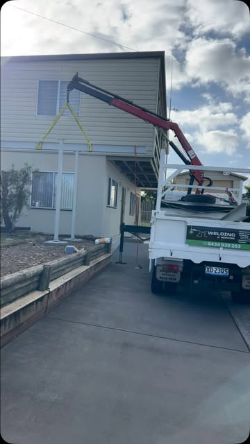 Hiab crane truck lifting a fabricated steel portal frame over a house during installation.