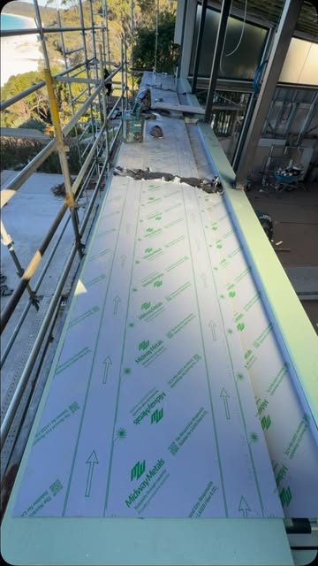 A long steel balcony capping still wearing its protective film, installed above a coastal deck.